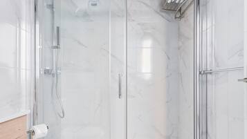 A modern bathroom with a glass-enclosed shower, a white toilet, and grey tiles.