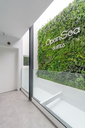 Entrada de hotel moderna com guarda-corpo de vidro, um jardim vertical verdejante e a inscrição 