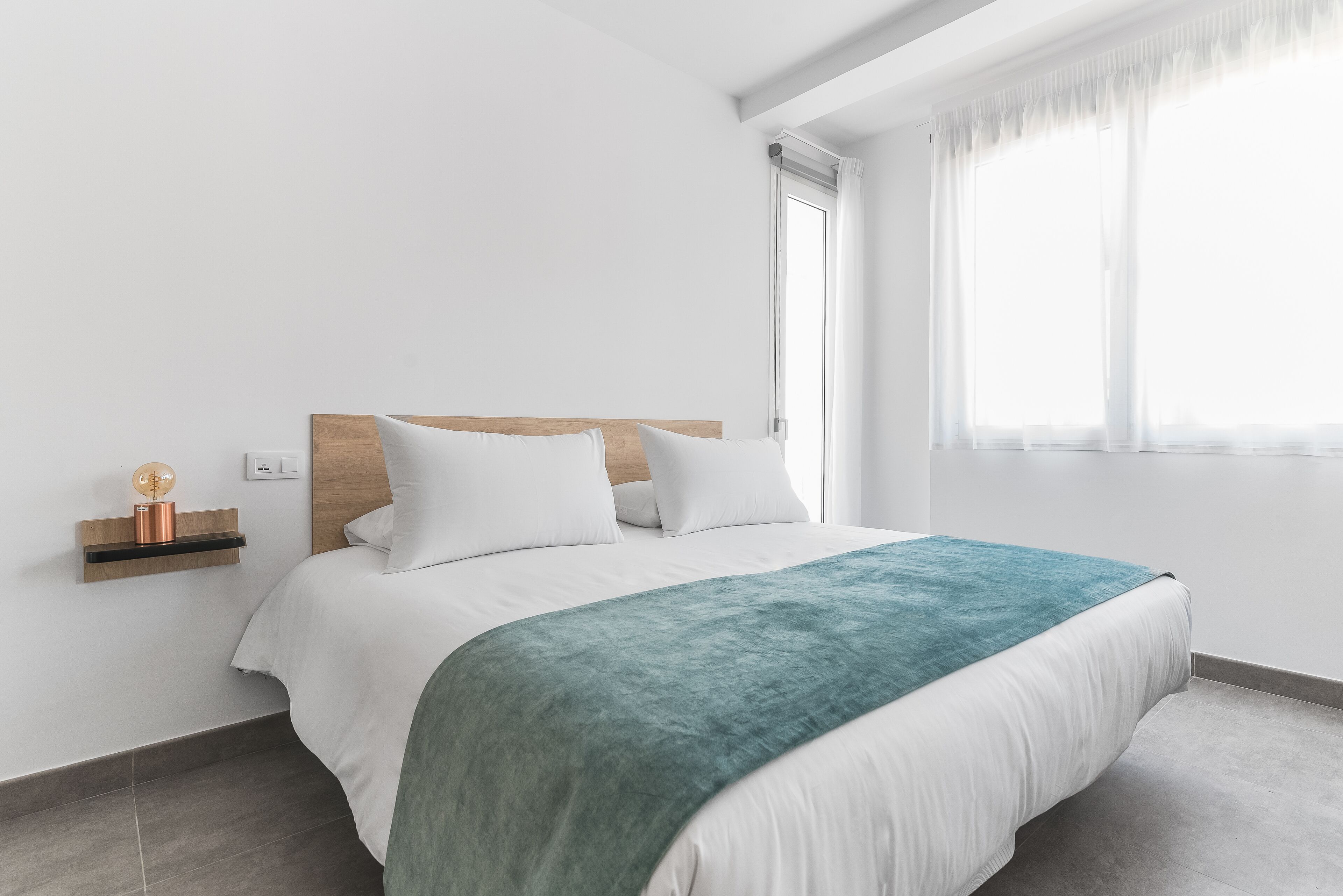 Un dormitorio moderno con cabecera de madera, ropa de cama blanca y una manta color turquesa.
