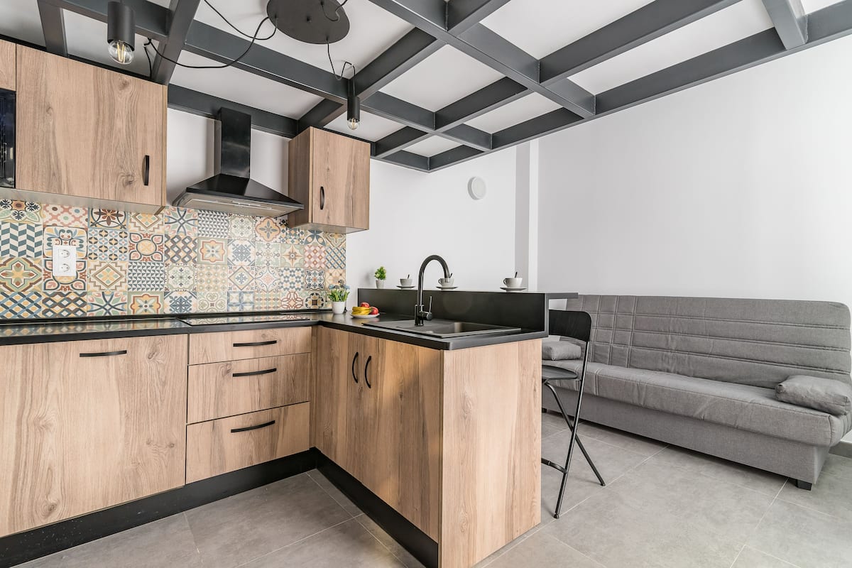 Una cocina moderna con armarios de madera, salpicadero de azulejos y un sofá gris en la zona de estar.