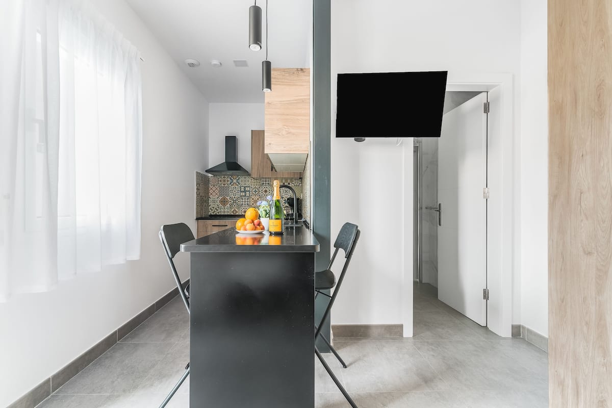 Una cocina moderna con una isla negra, dos sillas, un televisor montado en la pared y vistas al área de comedor.
