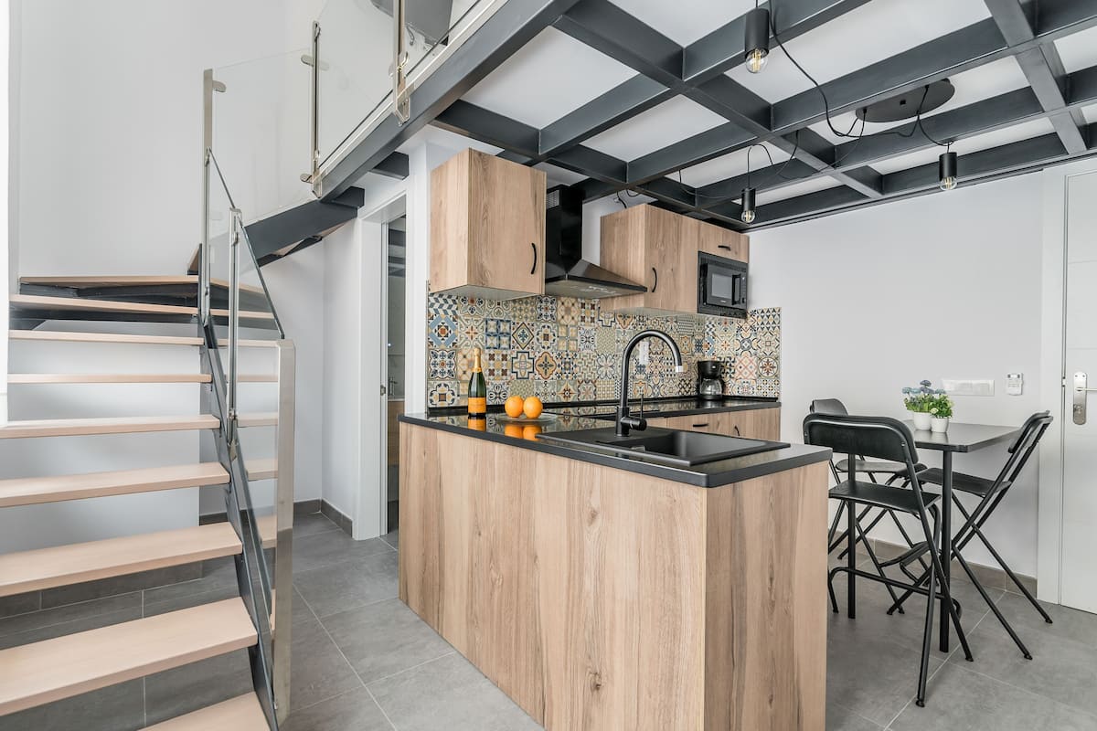 Una cocina moderna con una isla de madera, encimeras negras y un salpicadero de azulejos.