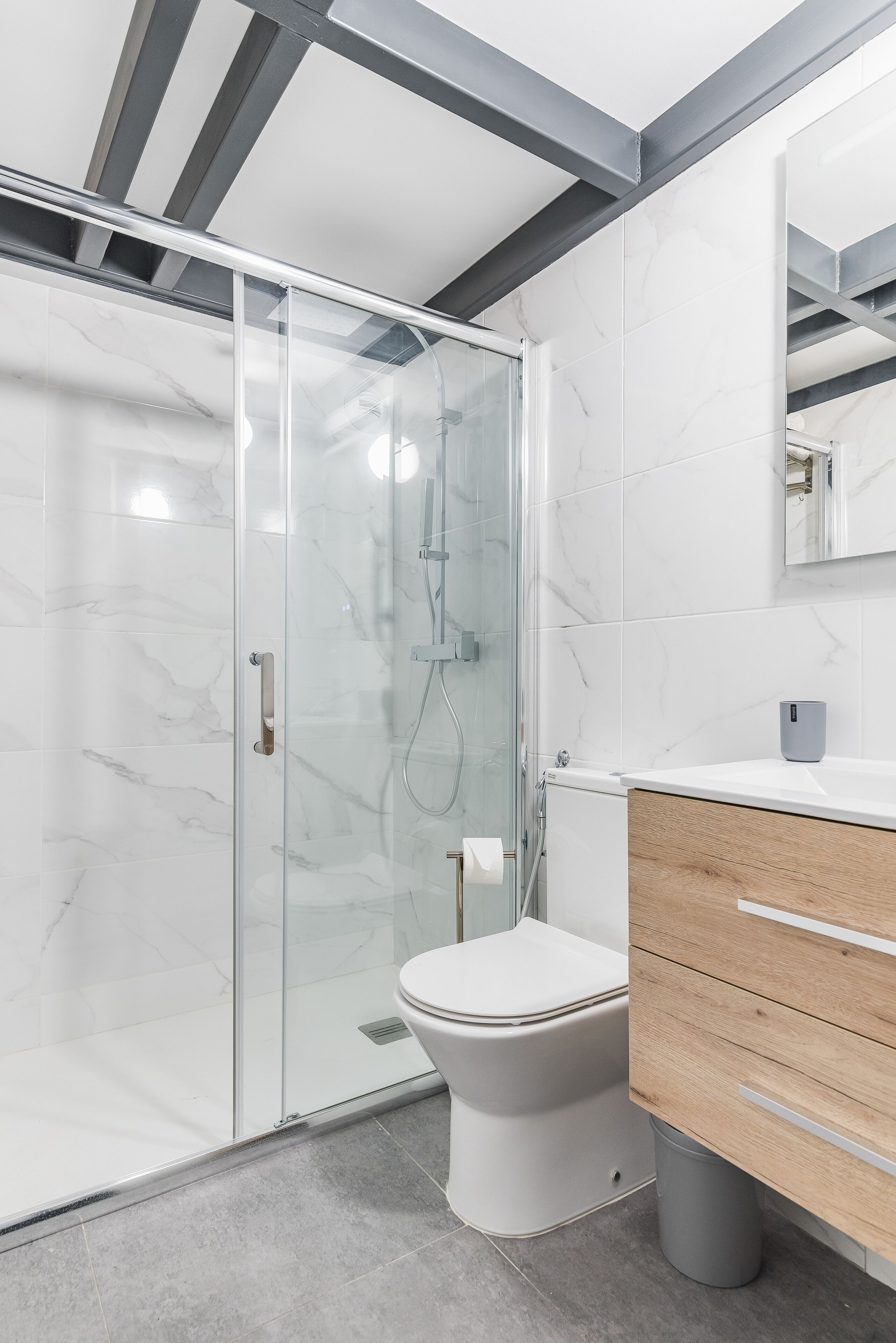 Un baño moderno con cabina de ducha de vidrio, inodoro blanco y tocador de madera con espejo.