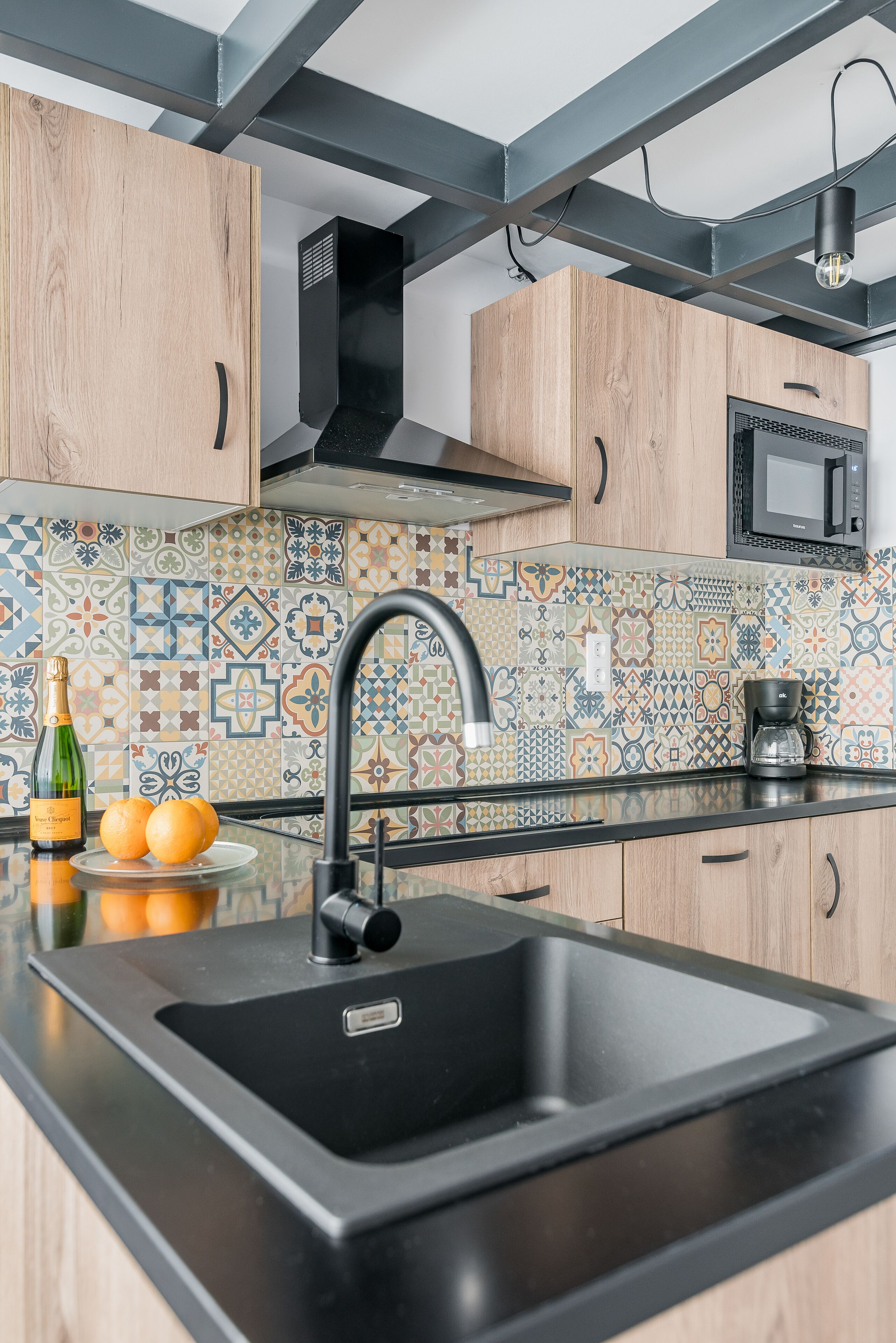 A kitchen with a black sink, wooden cabinets, a microwave, and a patterned backsplash.