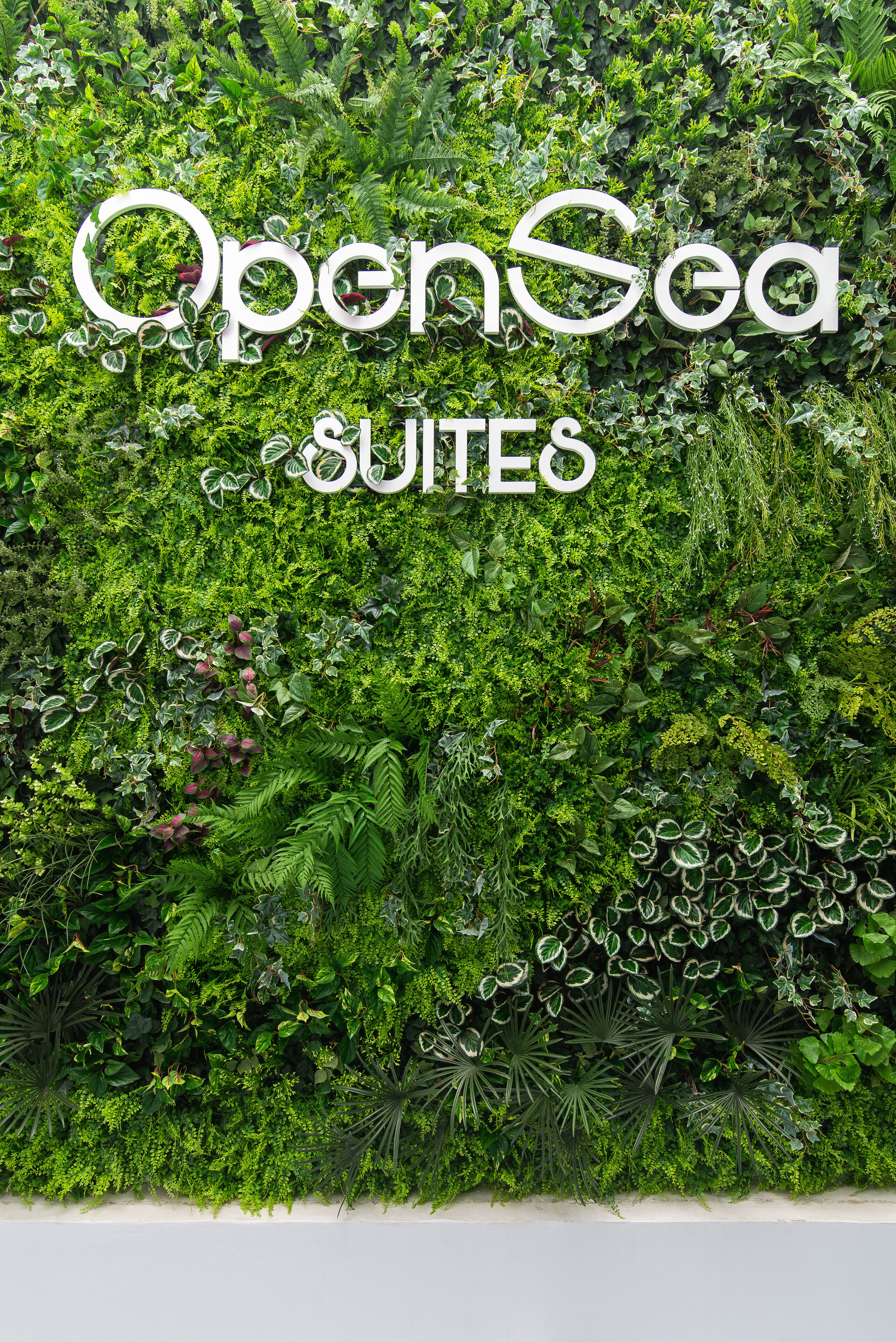 Una pared con el texto "OpenSea SUITES" en medio de una exuberante vegetación.