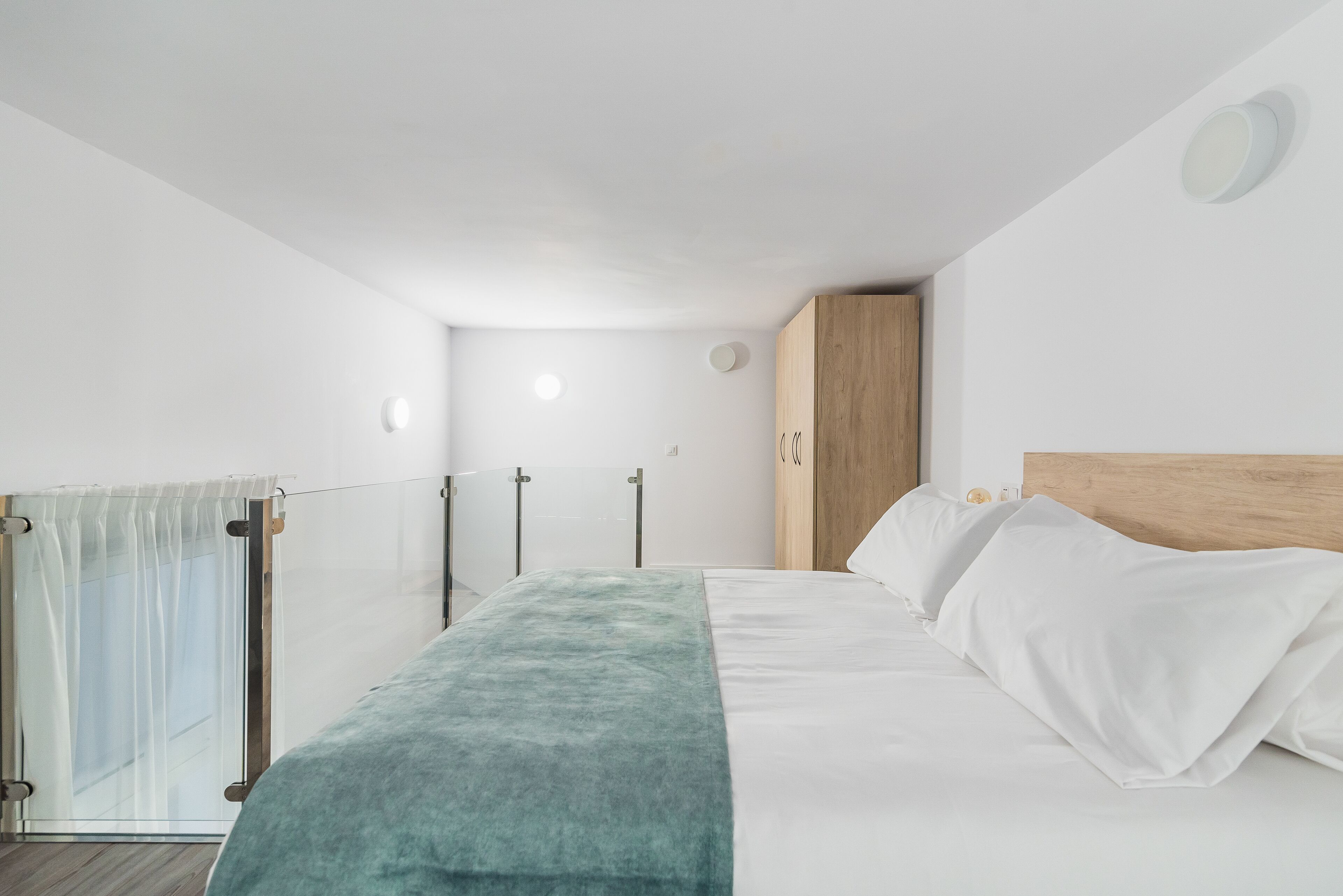 Un dormitorio moderno con una cama, un armario de madera y un ventanal de vidrio que da a un balcón.