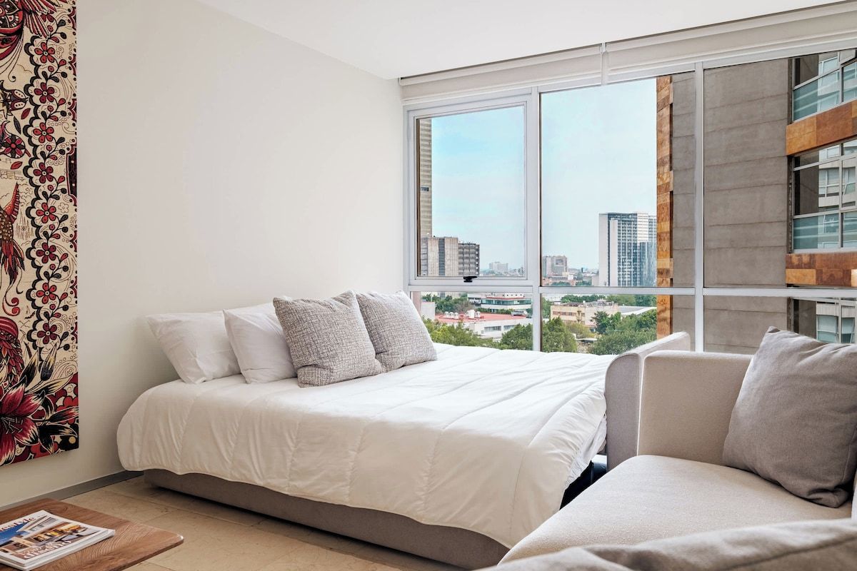 Une chambre moderne avec un lit, un canapé et une grande fenêtre donnant sur la ville.