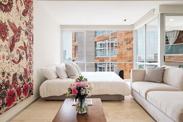 A modern bedroom with a large window, a bed, a sofa, and a coffee table.