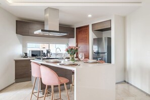 Cozinha moderna com ilha central, banquetas e geladeira de aço inoxidável.