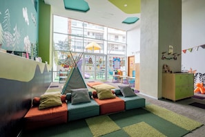 A children's play area with colorful seating, a slide, and a view of the outside.