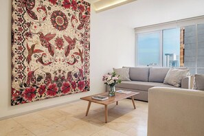 Una sala de estar con un cuadro floral grande en la pared, un sofá, una mesa de centro y un ventanal con vistas a la ciudad.