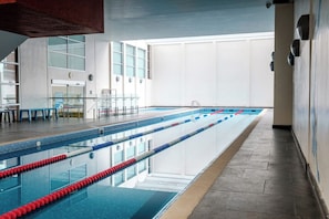 Piscina interna com pistas demarcadas, parede de vidro e design arquitetônico moderno.