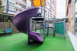 Um parquinho com um escorrega roxo, estruturas de escalada e uma lousa com letras.
