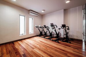 A room with wooden flooring, a row of stationary bikes, and two windows. - 1BR in Nuevo Polanco · Pool, Gym & Padel (Ciudad de México)
