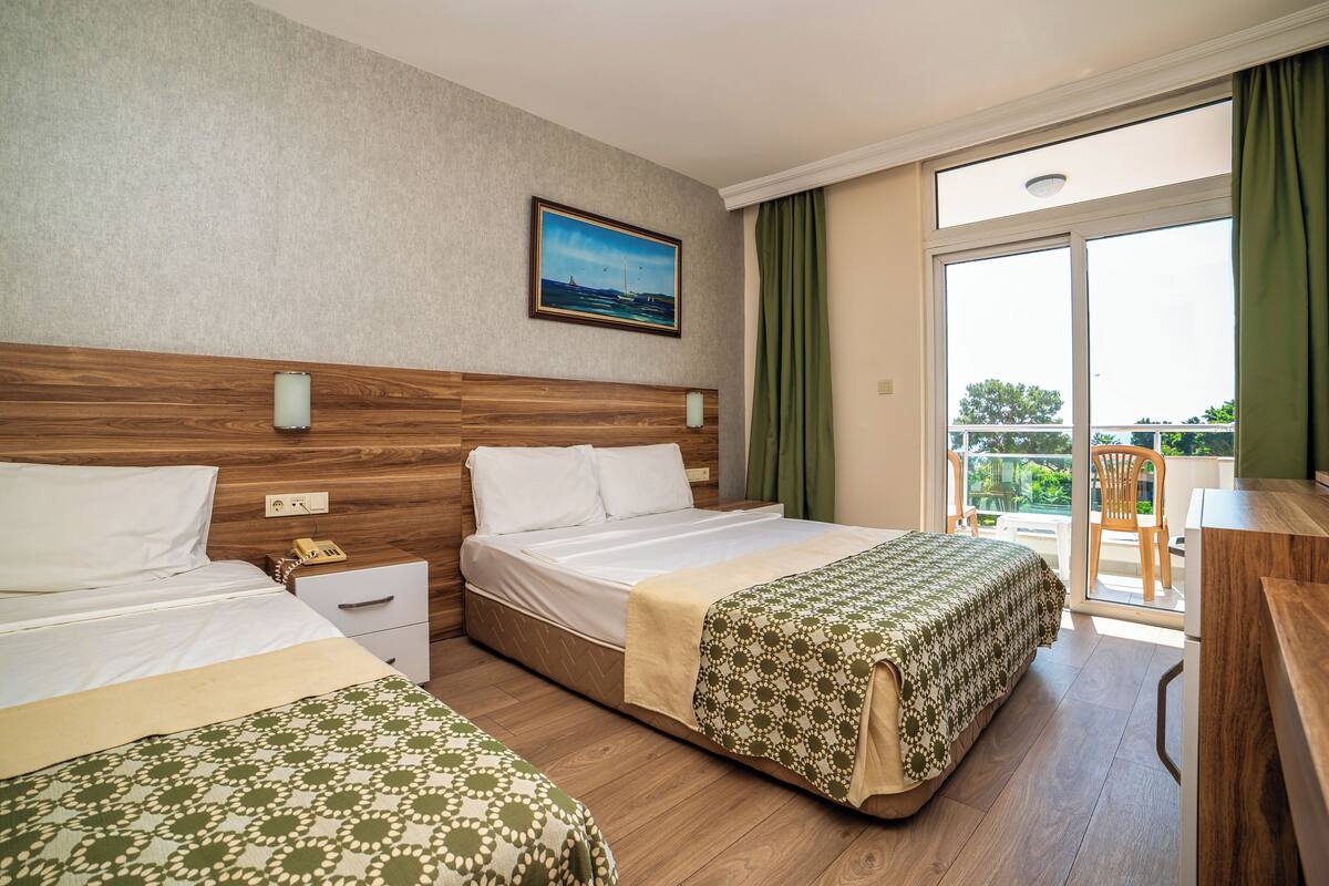 Habitación de hotel con dos camas, cabecera de madera, un cuadro, balcón con vistas y un escritorio con una silla.
