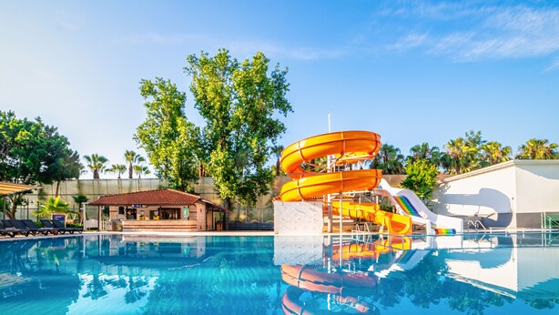 Una piscina con tobogán de agua, palmeras y un edificio con tejado de baldosas.