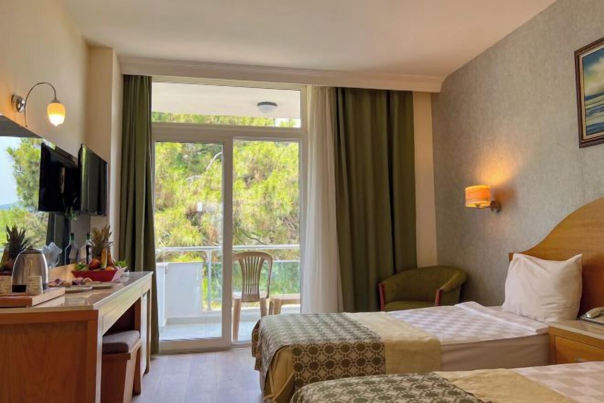 Habitación de hotel con dos camas, un escritorio con televisor y un balcón con una silla.