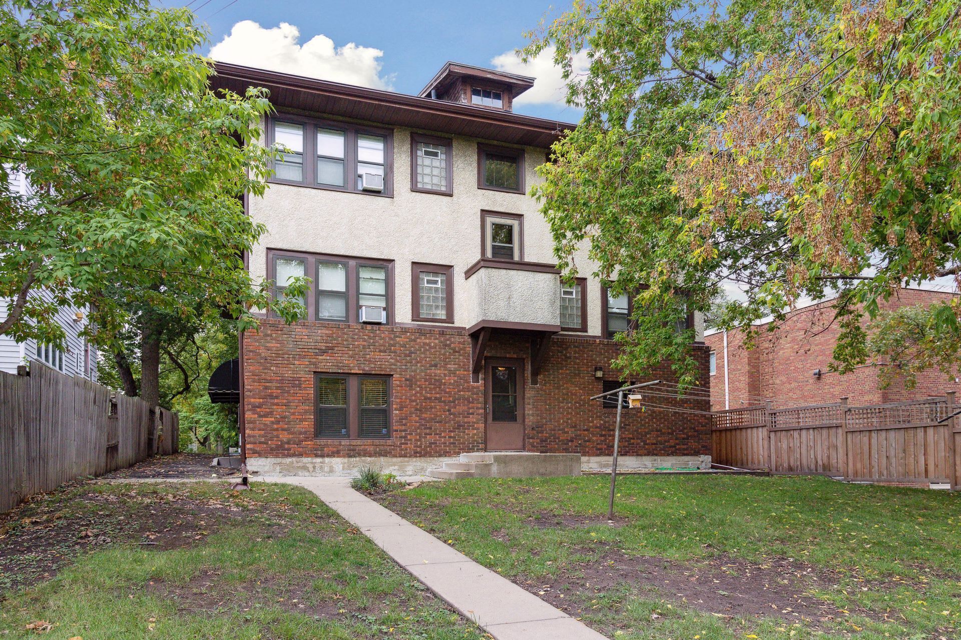 A two-story brick building with a central entrance, a small porch, and a visible air conditioning unit.