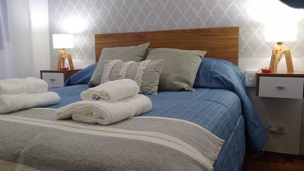 Ein ordentlich bezogenes Bett mit blau-weißer Bettwäsche, zwei Nachttische mit Lampen und eine Wand mit Muster.