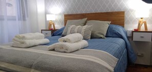 A neatly made bed with blue and white bedding, two bedside tables with lamps, and a patterned wall.