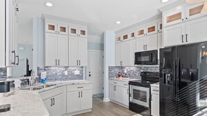 Una cucina moderna con mobili bianchi, un frigorifero nero, un forno a microonde e un piano cottura.