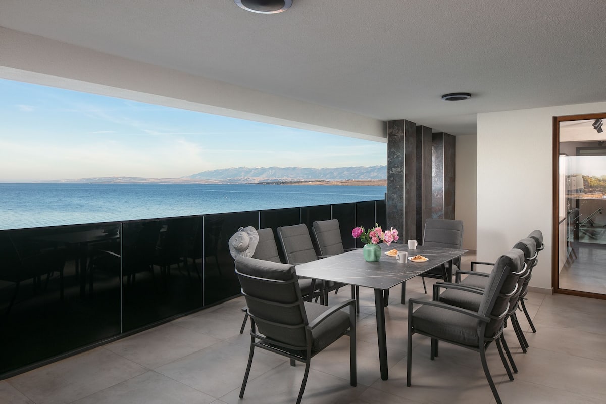 Ein Balkon mit Esstisch und Stühlen, Blick auf das Meer und modernes Interieur.