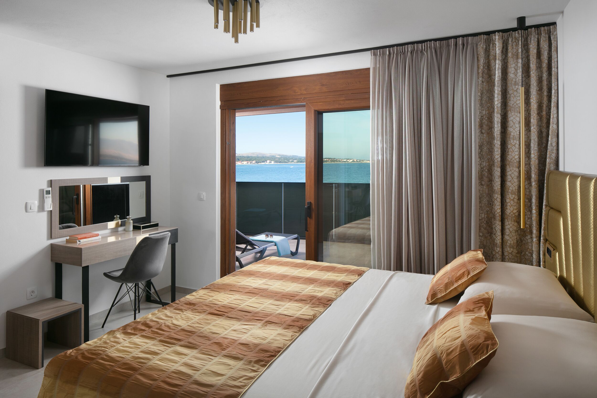 Ein Hotelzimmer mit Bett, Schreibtisch mit Stuhl, Fernseher und Balkon mit Meerblick.