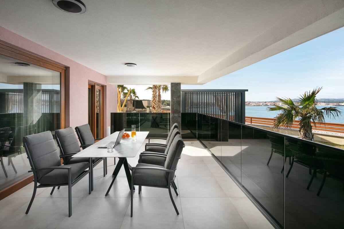 Ein moderner Essbereich mit großem Tisch und Stühlen, einer Glastrennwand und Blick auf das Meer.