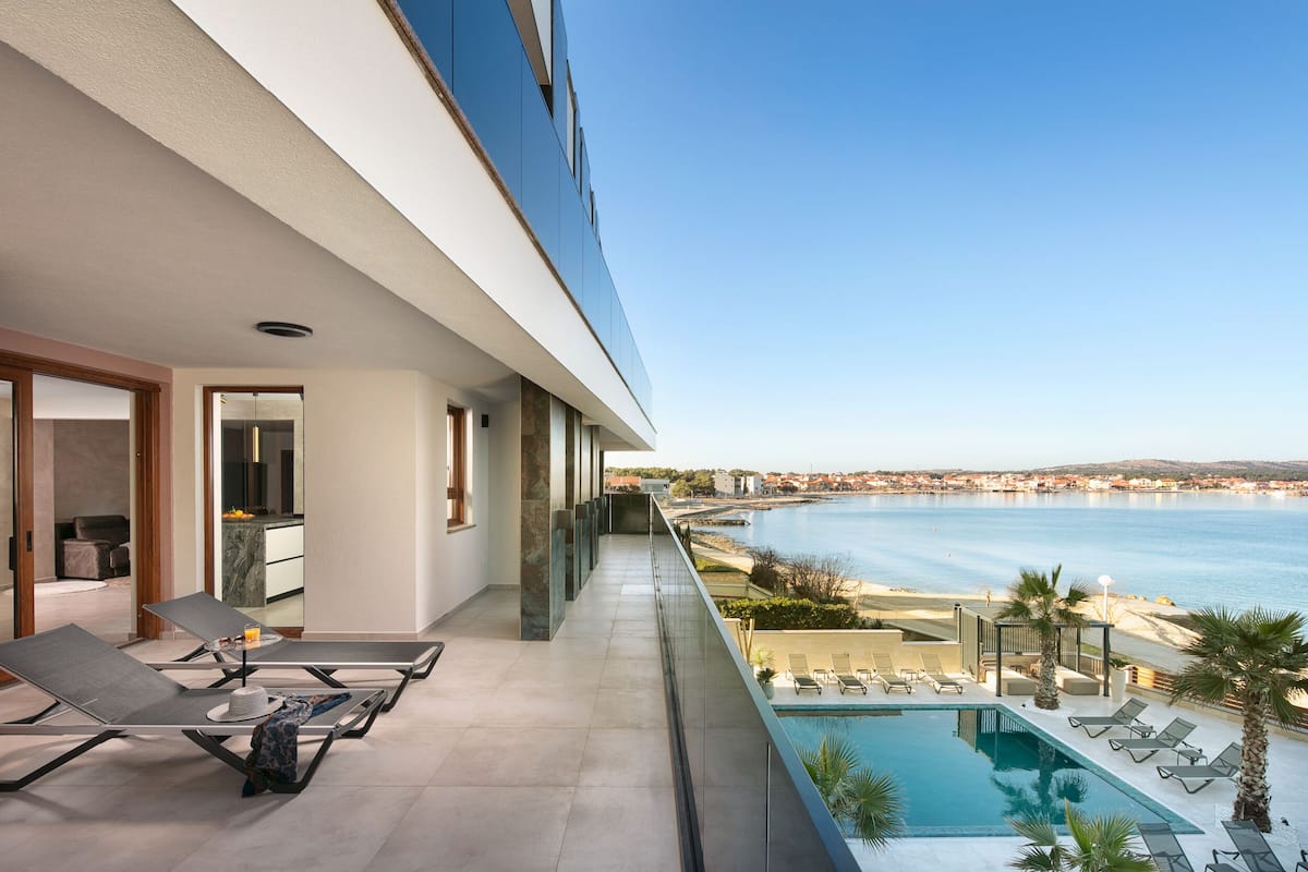 Ein moderner Hotelbalkon mit Pool, Liegestühlen und Meerblick.