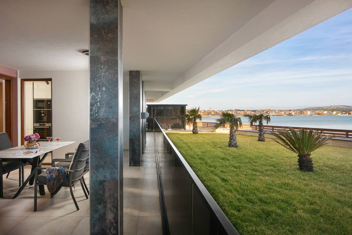 Ein moderner Balkon mit Meerblick, ein Essbereich mit Stühlen und Tisch sowie ein begrünter Außenbereich mit Palmen.