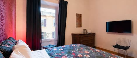 A bedroom with a bed, a dresser, a chair, a television, and a window with curtains.