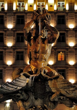 A bronze statue of a muscular figure with a flowing garment, set against a building facade with illuminated windows. - Rome La Sapienza Apartment (Rome)