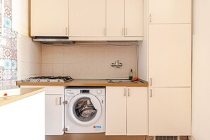 A compact kitchen with a washing machine, a gas stove, and a tiled backsplash. - Rome La Sapienza Apartment (Rome)