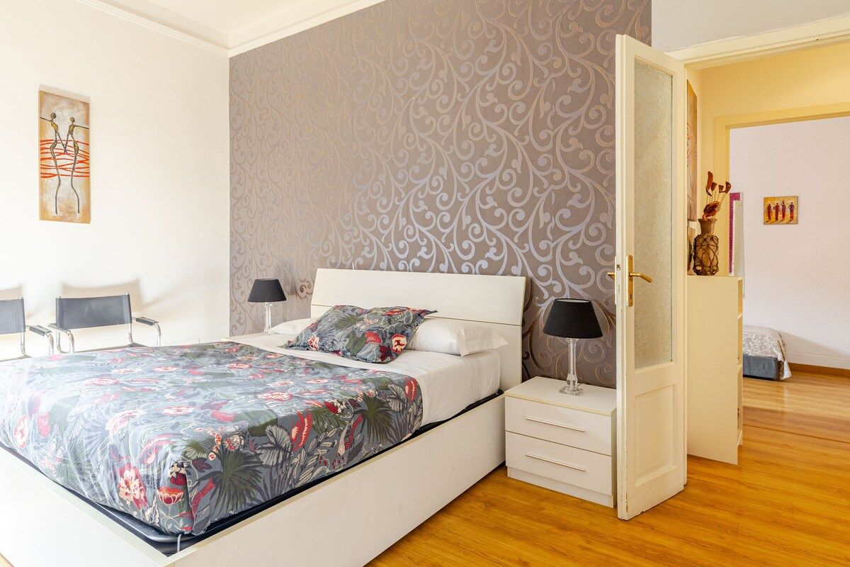 Une chambre à coucher comprenant un lit, des tables de chevet, une commode et une porte donnant sur une autre pièce.