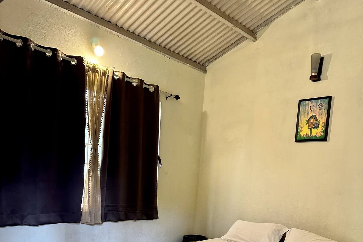 Een slaapkamer met een houten bed, wit beddengoed, een raam met gordijnen, een wandlamp en een lijst met een foto.