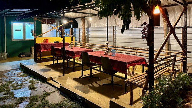 Un espace repas avec des tables et des chaises, une structure en bambou et un petit bâtiment en arrière-plan.