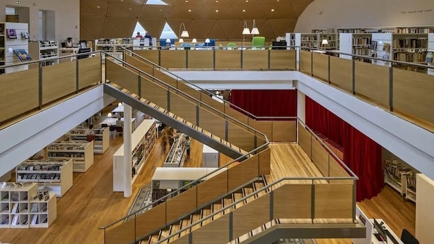 Een bibliotheek met meerdere verdiepingen, een geometrisch plafondontwerp, houten vloeren en een centrale trap.
