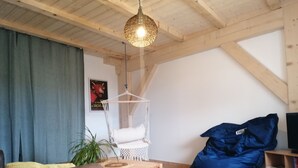 Uma sala de estar acolhedora com teto de madeira, luminária pendente, mesa de madeira, um bean bag e uma estante de livros.