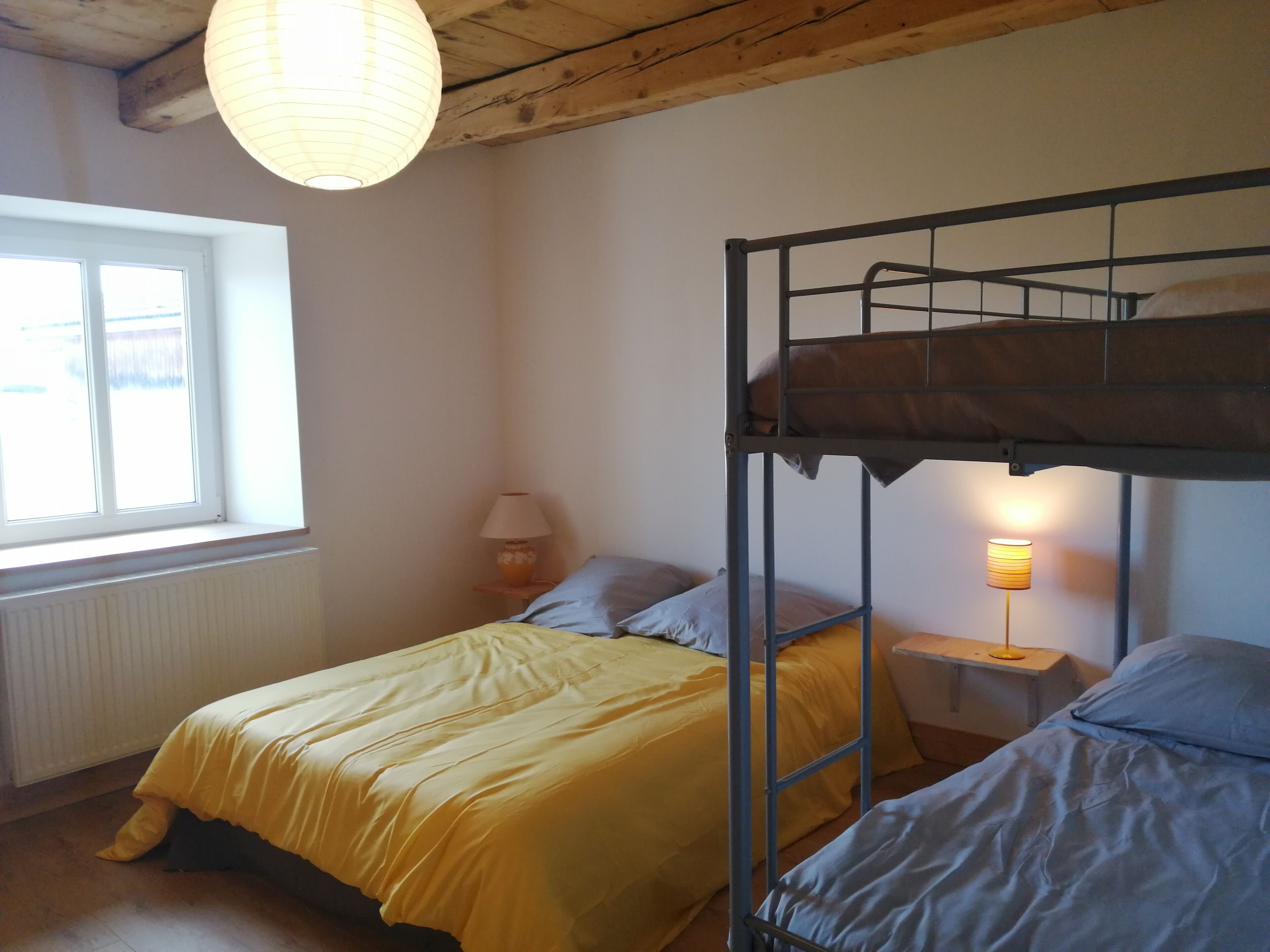 Ein Schlafsaalzimmer mit Etagenbetten, einem Fenster, einer Lampe und einer Heizung.