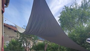 Een terras buiten met een tafel, stoelen, een barbecue en een zonnescherm.