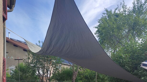 Un patio al aire libre con mesa, sillas, una parrilla y un toldo de sombra.