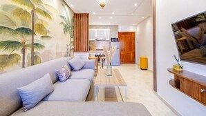 Ein modernes Wohnzimmer mit einer Couch, einem Couchtisch, einem Fernseher und einer Küche im Hintergrund.