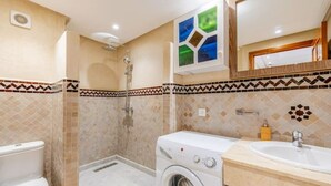 Ein Badezimmer mit Dusche, Toilette, Waschmaschine und Waschbecken.