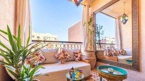 Ein Balkon mit einer Couch, einem kleinen Tisch, einem Blumentopf und einem dekorativen Spiegel.