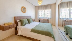 Ein Schlafzimmer mit Bett, Nachttisch, Spiegel und Fenstern.