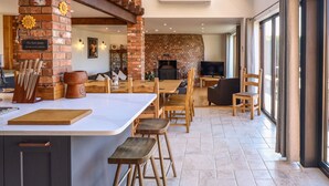 A modern kitchen with a large island, bar stools, and a brick wall. - Brambleberry Barn (Spilsby)