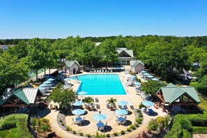 Ein Resort mit einem zentralen Schwimmbad, Liegebereichen mit Sonnenschirmen und verschiedenen Sitzgelegenheiten im Freien.