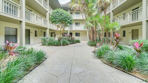 A multi-story building with a central courtyard featuring a geometric-patterned walkway, surrounded by lush greenery and palm trees. - Bonita Springs Condo w/ Community Pool! (Bonita Springs)