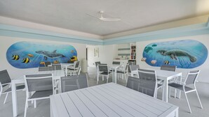 A room with white tables and chairs, a ceiling fan, and murals of marine life on the walls. - Bonita Springs Condo w/ Community Pool! (Bonita Springs)