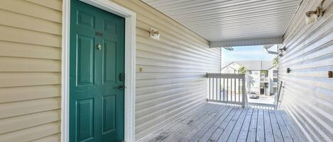 A wooden porch with a green door, a white railing, and a clear view of the street and buildings in the background.